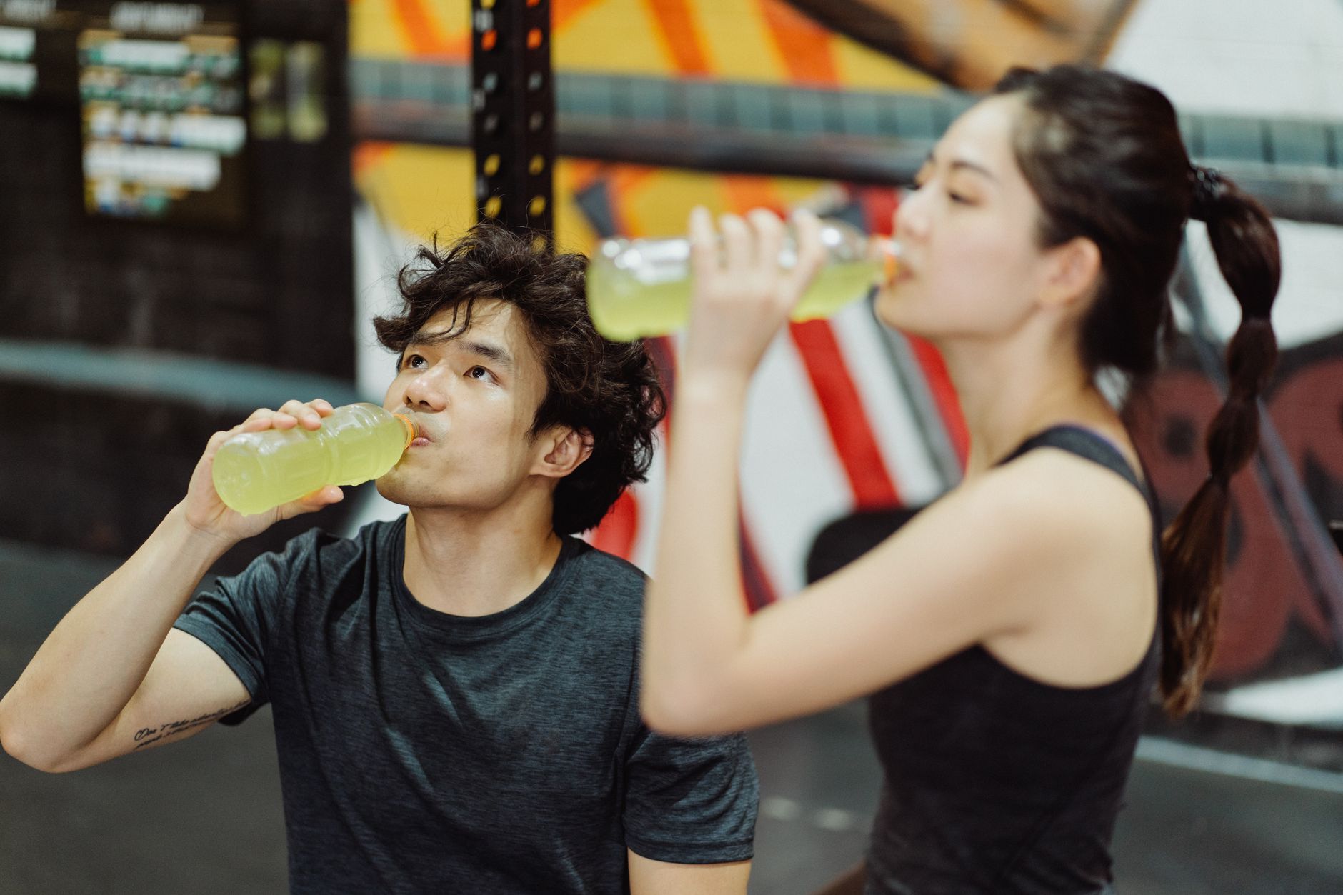 Two people drinking from water bottles after a workout in a gym